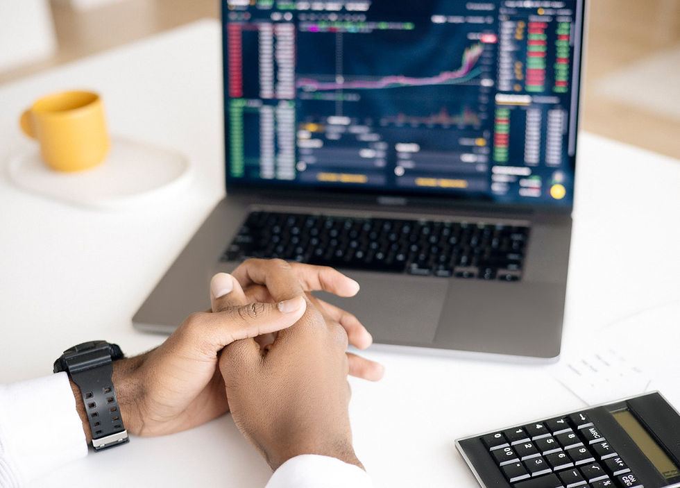 Cmputer with multicolor graphics on the screen, two man hands intertwined in each other and a calculator on the right, all on a white table, plus a yello mug on the left side of the photo, unfocused