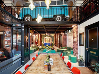 Intérieur coloré avec un van bleu en mezzanine, déco rétro, canapés verts, table en bois avec chaises rouges, ambiance conviviale.