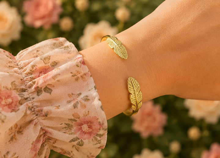 Thumbnail: 18K Gold Plated Feather Bangle on a women's wrist in a rose garden