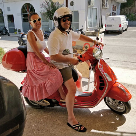 couple smilling while possing on an orange GTS Vespa in Corfu town