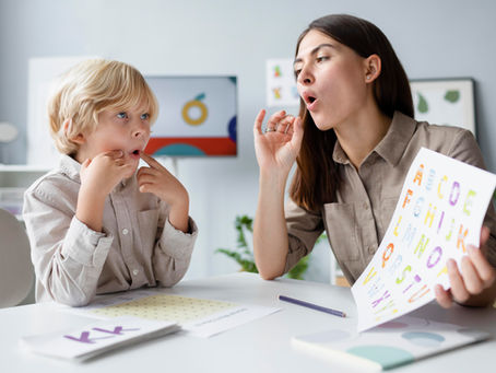Childcare teacher helping a young child practice speech and letter sounds using an alphabet learning worksheet at My Kid's Daycare in Houston, TX, supporting early language development and preschool readiness