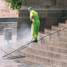Worker in green uniform pressure washing stone stairs