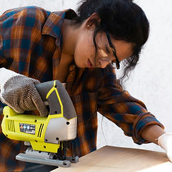 Woman wearing safety glasses and gloves operates a jigsaw to cut wood