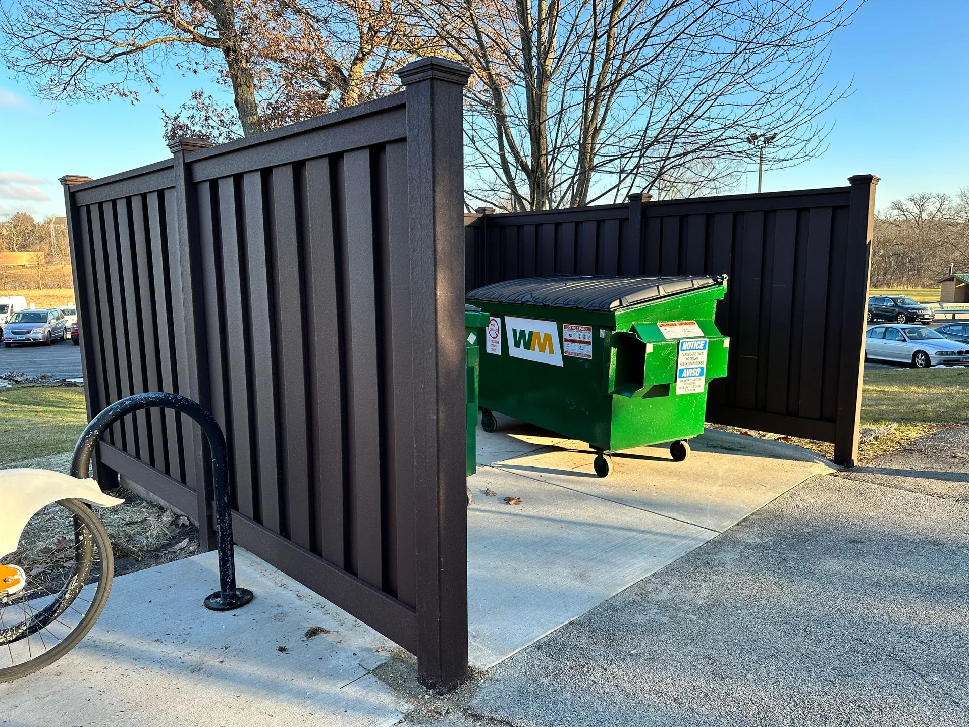 Green dumpster behind a dark privacy fence with a bike rack
