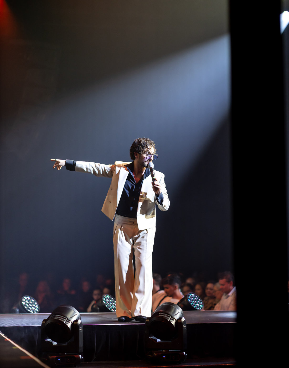 Benny Gregs on stage in a white suit, pointing to the crowd