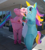 two inflatable unicorns of blue and pink dance with a pride flag at a pride event in sonoma county.