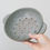 Thumbnail: Hand holding grey stoneware fruit bowl with holes for draining pasta.