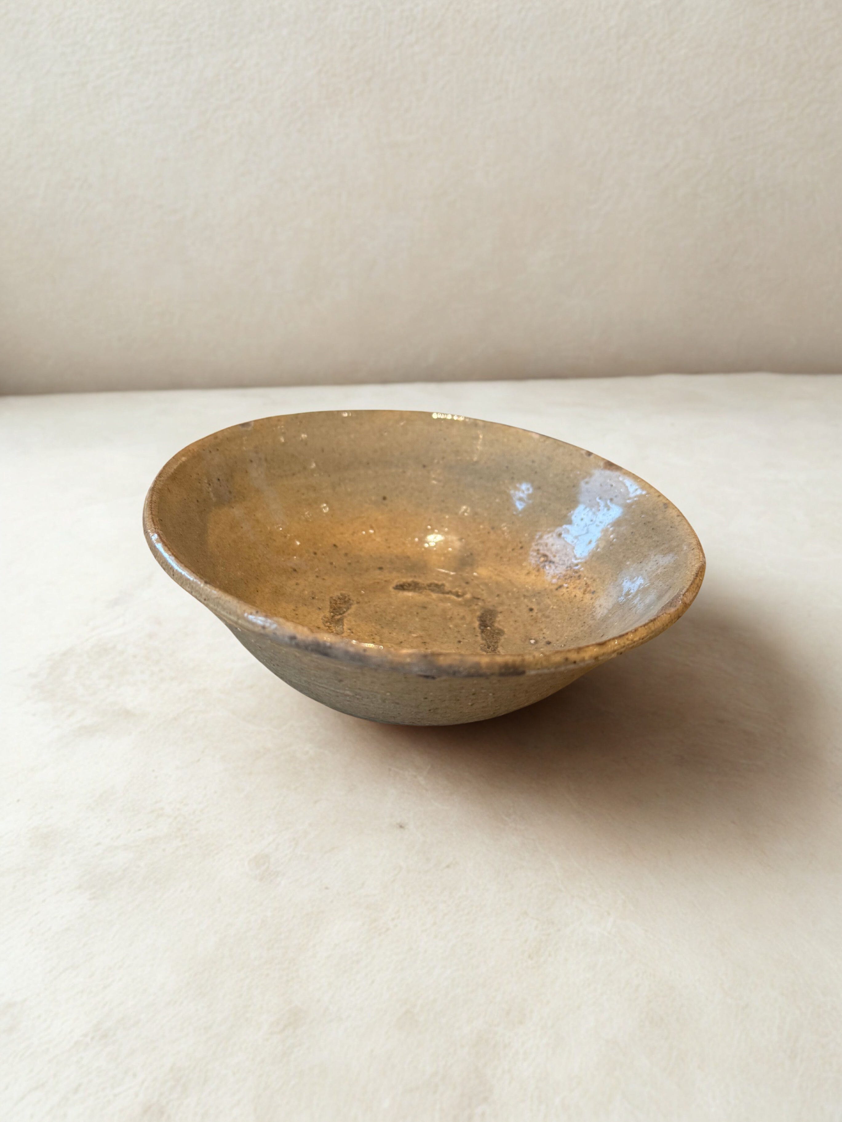 Rustic ceramic bowl, beige color, resting on a flat, light-colored surface.