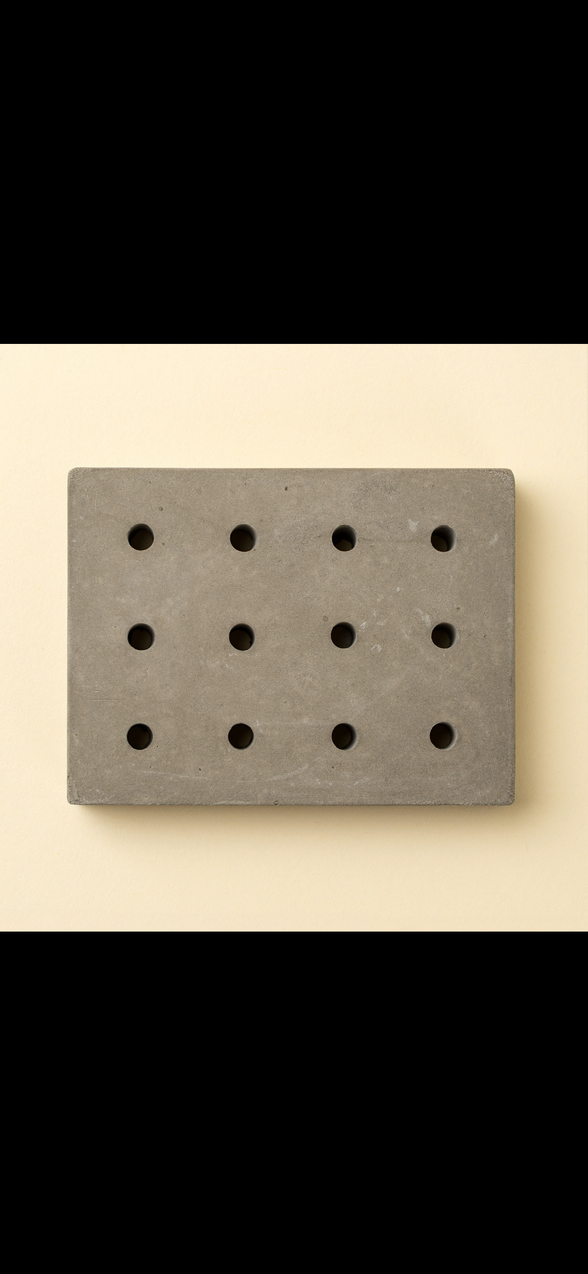 Gray rectangular concrete soap dish with holes on cream background.