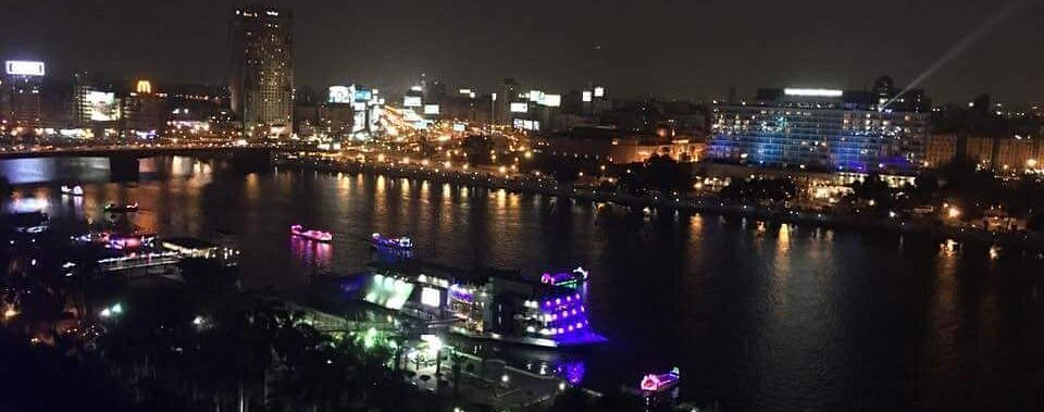 Tourists standing by the railing of a Nile dinner cruise ship, enjoying the fresh breeze and nighttime views of Cairo