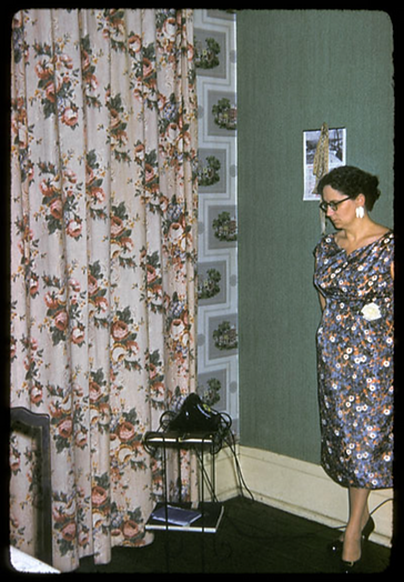 Woman in a 1960's setting near phone and curtain