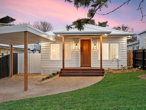 Modern white house with wooden door, carport, and lawn at sunset.