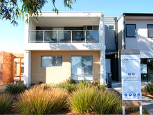Modern two-story house with a glass balcony, beige brick facade, surrounded by greenery. A Key Housing Group sign is in front.