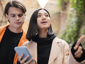 Two people in a leafy alley, woman in beige coat points while holding a phone; man in orange jacket looks down. Driftscape logo.