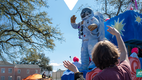 Parade float with a white-suited astronaut, people reaching up, blue platform, trees and sky; Driftscape digital tourism app logo.