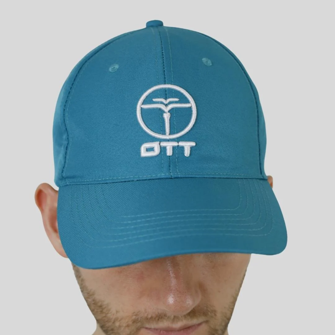 A man wearing a blue cap with a white circular logo and the letters OTT on the front, looking down with his face partially visible.