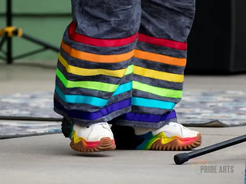 Two legs, one slightly lifted off the ground, on stage wearing ranbow ribbon pants and rainbow sneakers