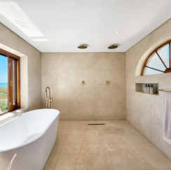 Luxury bathroom featuring a white freestanding tub, walk-in shower and ocean views through a high arched window at a Cape Town villa.