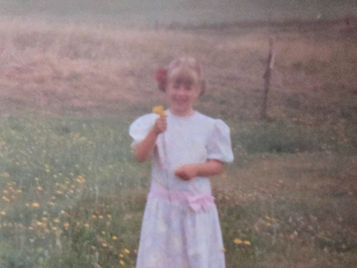 Little girl in a dress standing in a field holding dandelions and smiling
