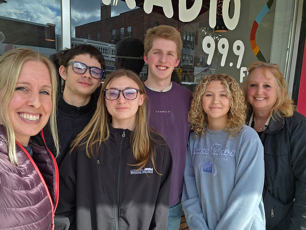 Group of six people smiling outside a radio station, with "RADIO 99.9" visible. Casual attire, sunny day, and cheerful mood.