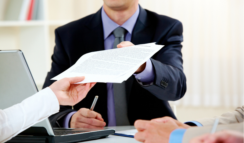 a man in a suit is handing a piece of paper to another man
