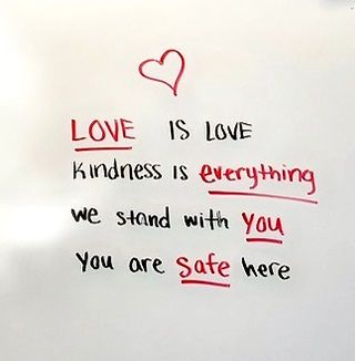 On a teacher's whiteboard is written the text "Love is love, kindness is everything, we stand with you, you are safe here"