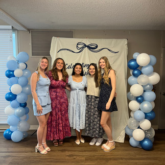 Small group of women posing in front of banner and balloons