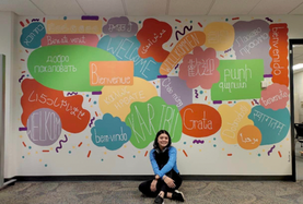 Woman in front of a colorful mural with 'WELCOME' in many languages