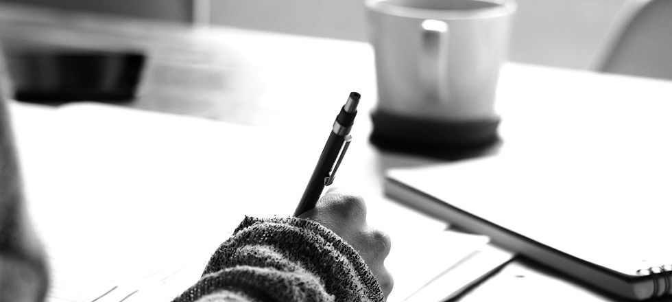Hand writing with a pen, coffee mug nearby