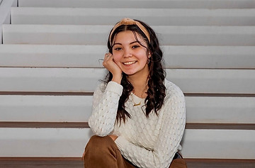 Girl with long brown hair posed sitting on steps inside with white sweater