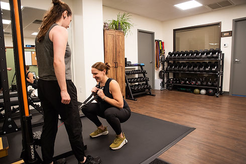 Pregnant woman prefroming a squat as a part of her prenatal strengthening program at Keep It Moving Physical Therapy and Wellness in Burlington MA with her personal trainer