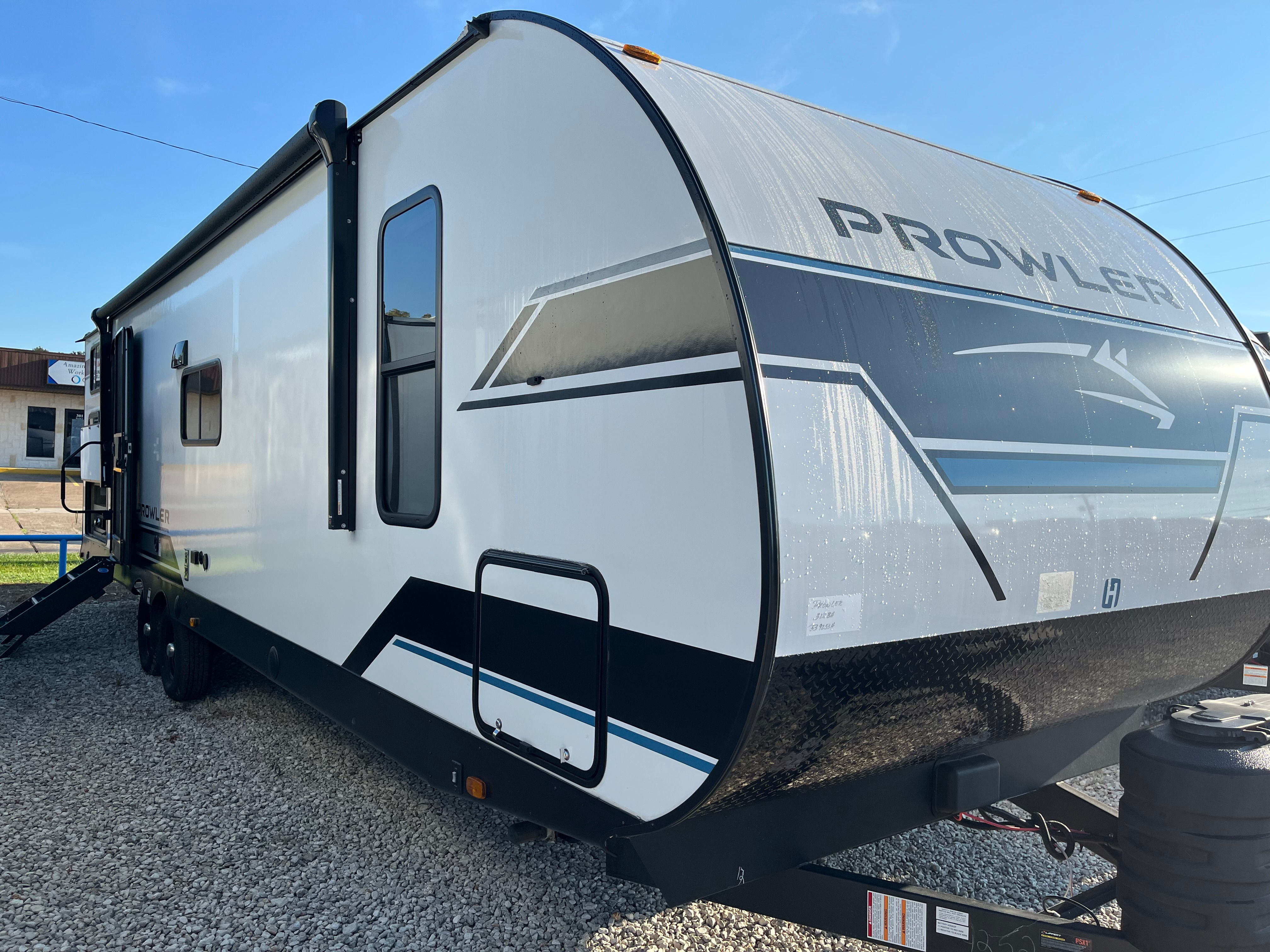White Prowler RV trailer parked outdoors with blue accents. LOCAL RV DEALERSHIP.