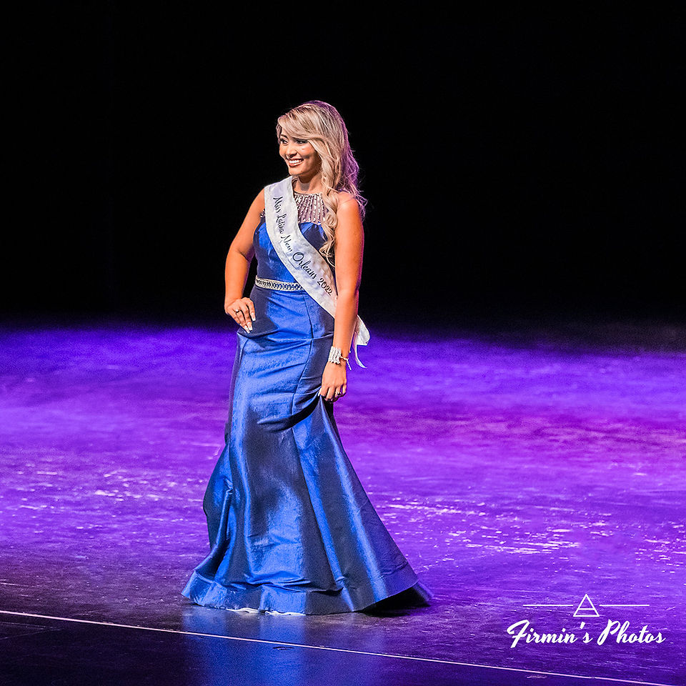 Woman wearing a blue dress while standing on stage wearing a New Orleans, Louisiana event sash