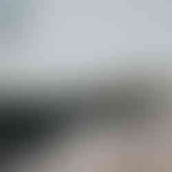 Family of six sitting on a beach at sunset, smiling. Parents hold a baby, surrounded by three kids. Rocky shore and calm water in background. Hawaii island beach photographer