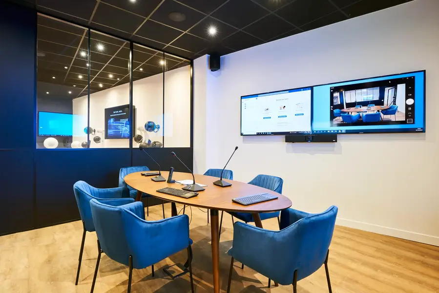 Salle de réunion avec écran double, barre de visioconférence et microphones pupitres
