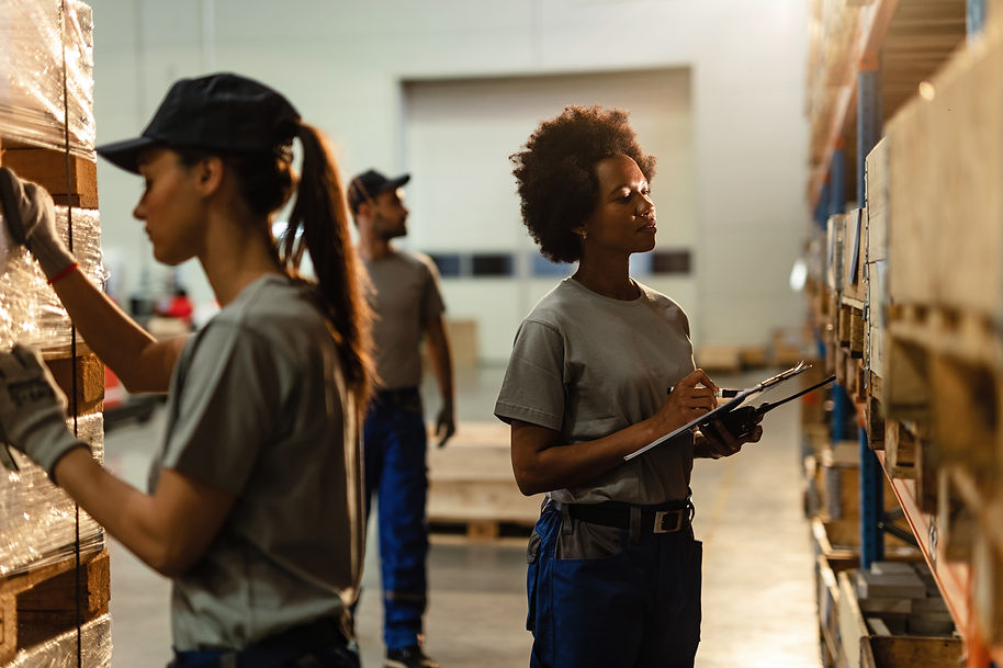 black-female-warehouse-worker-going-through-shipment-list-while-checking-stock-industrial-