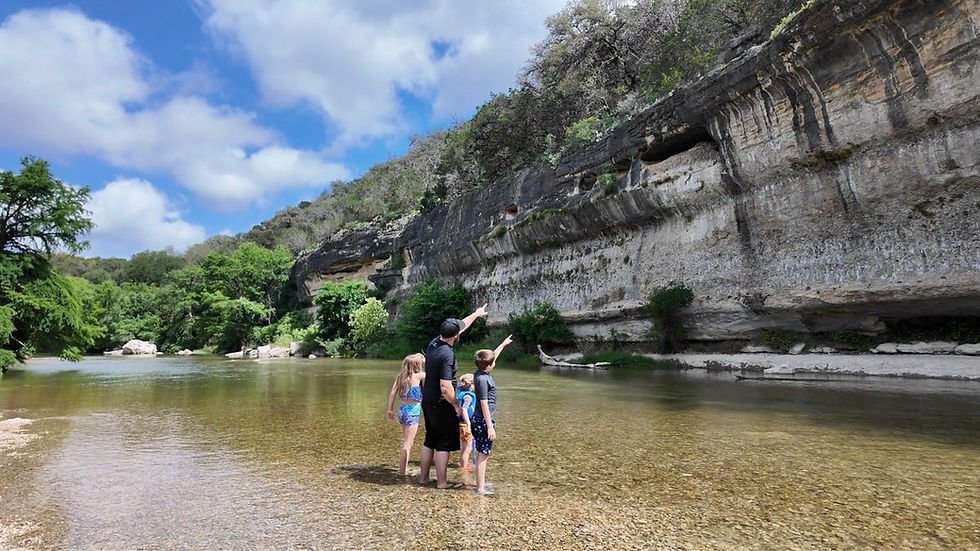 Family standing in the Guadalupe River looking at limestone cliffs at Guadalupe River State Park in Texas.