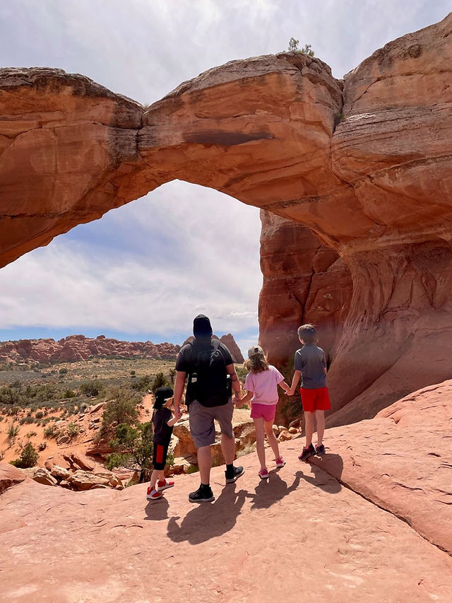 Family hiking toward a natural arch in Arches National Park, Utah.
