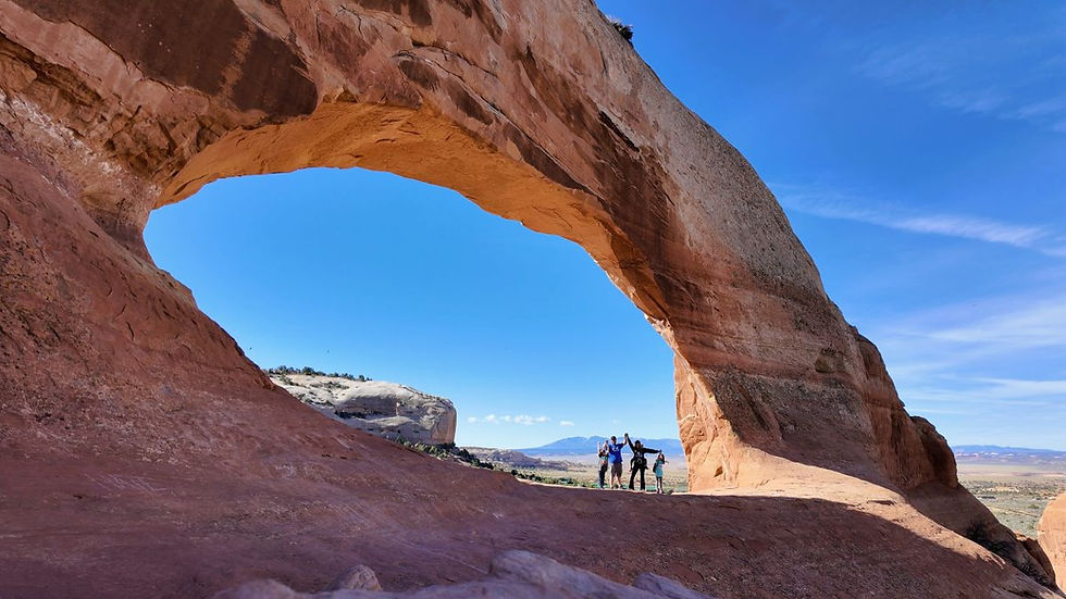 Family standing under a large natural rock arch (Wilson Arch) near Moab, Utah.
