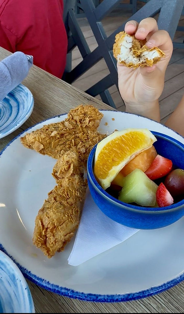 Corn flake crusted American red snapper fish sticks with fresh fruit from the kids menu.