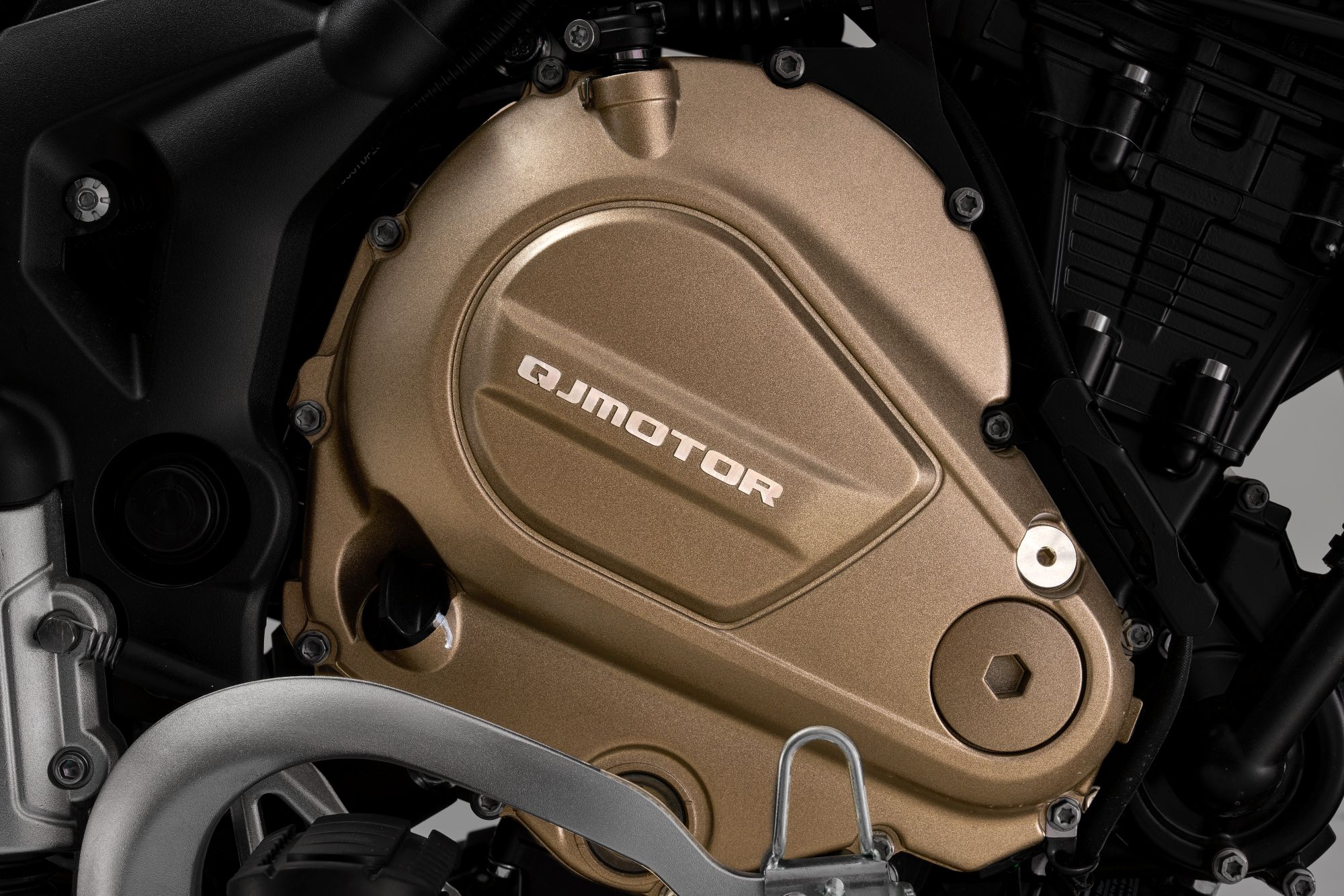 QJMOTOR SRT 700 SX: Nahaufnahme des bronzefarbenen Motorblocks mit Krümmer und Rahmen.