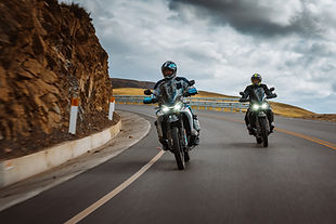 Zwei Fahrer stehen mit einer blauen und einer schwarzen CFMOTO 800MT-X vor einem warm beleuchteten Hintergrund.