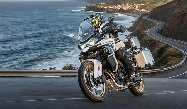 Fahrer auf einer weißen CFMOTO 800MT-ES auf einer kurvigen Straße an der Küste.