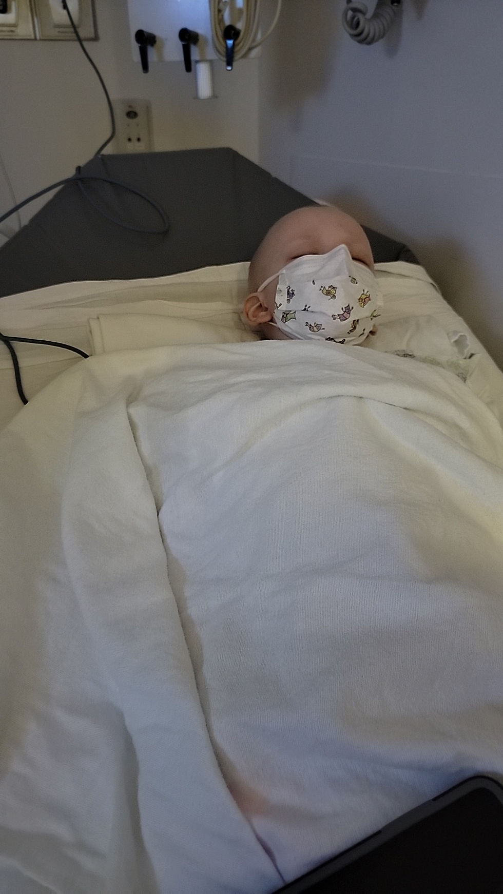 Adeline is laying eyes closed covered in blankets with her mask on while we wait at Children's Hospital ER.