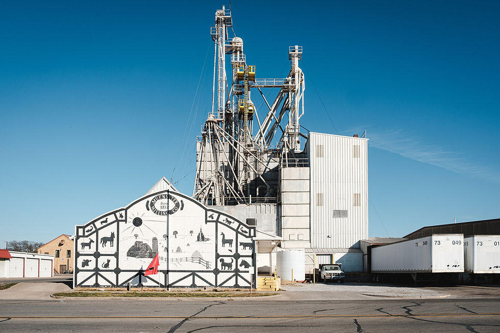 white building with black farm illustrations in front of an industrial feed mill