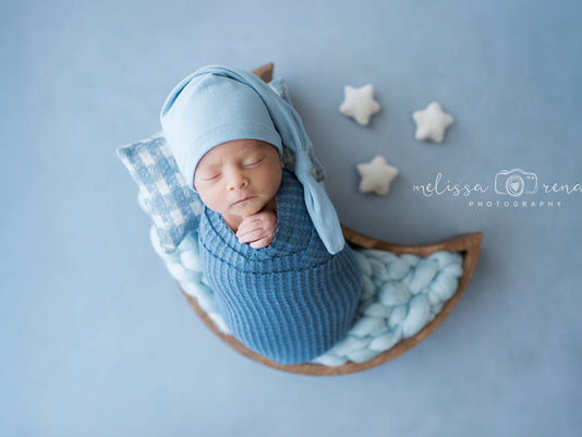 Sleeping baby in blue hat and wrap on crescent-shaped cushion, with stars and blue background. Text: Melissa Renae Photography. Calm mood in Phoenix Arizona.