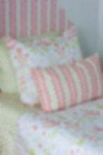 Bed made up in pink, coral and gold patterns of floral and stripes