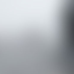 A imagem mostra uma estrada com tráfego intenso em meio à neblina e pista molhada, indicando condições climáticas adversas, como chuva ou garoa forte. Veículos de passeio e caminhões seguem em ambas as direções, com visibilidade reduzida e marcas d’água no asfalto. A cena transmite uma sensação de atenção, risco e necessidade de direção cuidadosa em dias chuvosos ou com baixa visibilidade.