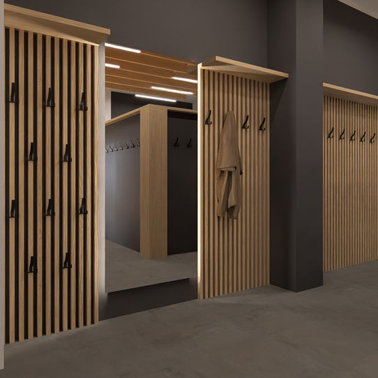 3D vizualizace šatny v minimalistickém stylu. Stěnám dominuje tmavě šedá výmalba a obklady ze svislých dřevěných lamel, na kterých jsou připevněny černé kovové háčky na kabáty. Uprostřed je velké zrcadlo, které opticky zvětšuje prostor a odráží protější lamelovou stěnu a visící zelené rostliny. Na podlaze je položena tmavě šedá velkoformátová dlažba.