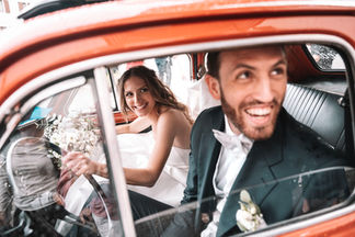 Sposi ridono dentro un'auto d'epoca rossa decorata con fiori
